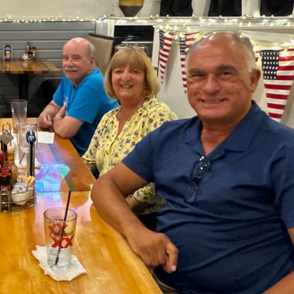 Three smiling customers seated at a wooden bar counter with American flag bunting in the background.