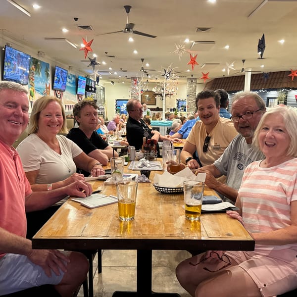 Six smiling people seated around a wooden table with drinks at The Salted Rim Margarita Bar & Grille.