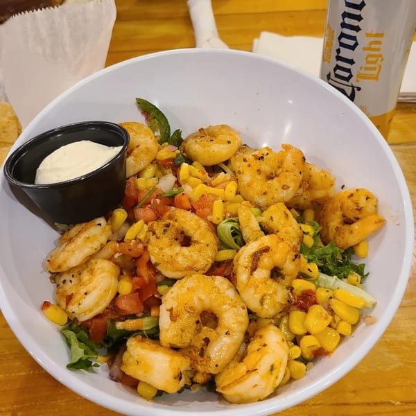 A shrimp salad with corn, tomatoes, and lettuce, served with a side of sour cream and a Corona Light.