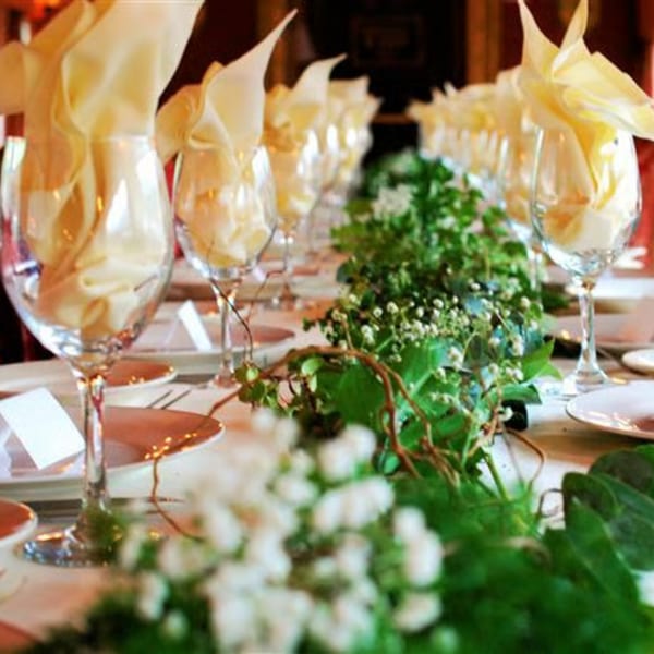 Elegantly set long dining table with wine glasses, gold napkins, and a lush green floral runner.