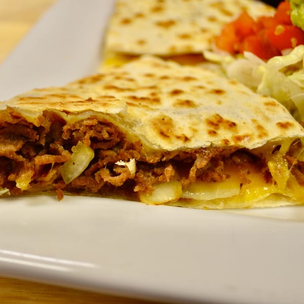 Close-up of a quesadilla cut in half, revealing a savory filling of meat, onions, and melted cheese.