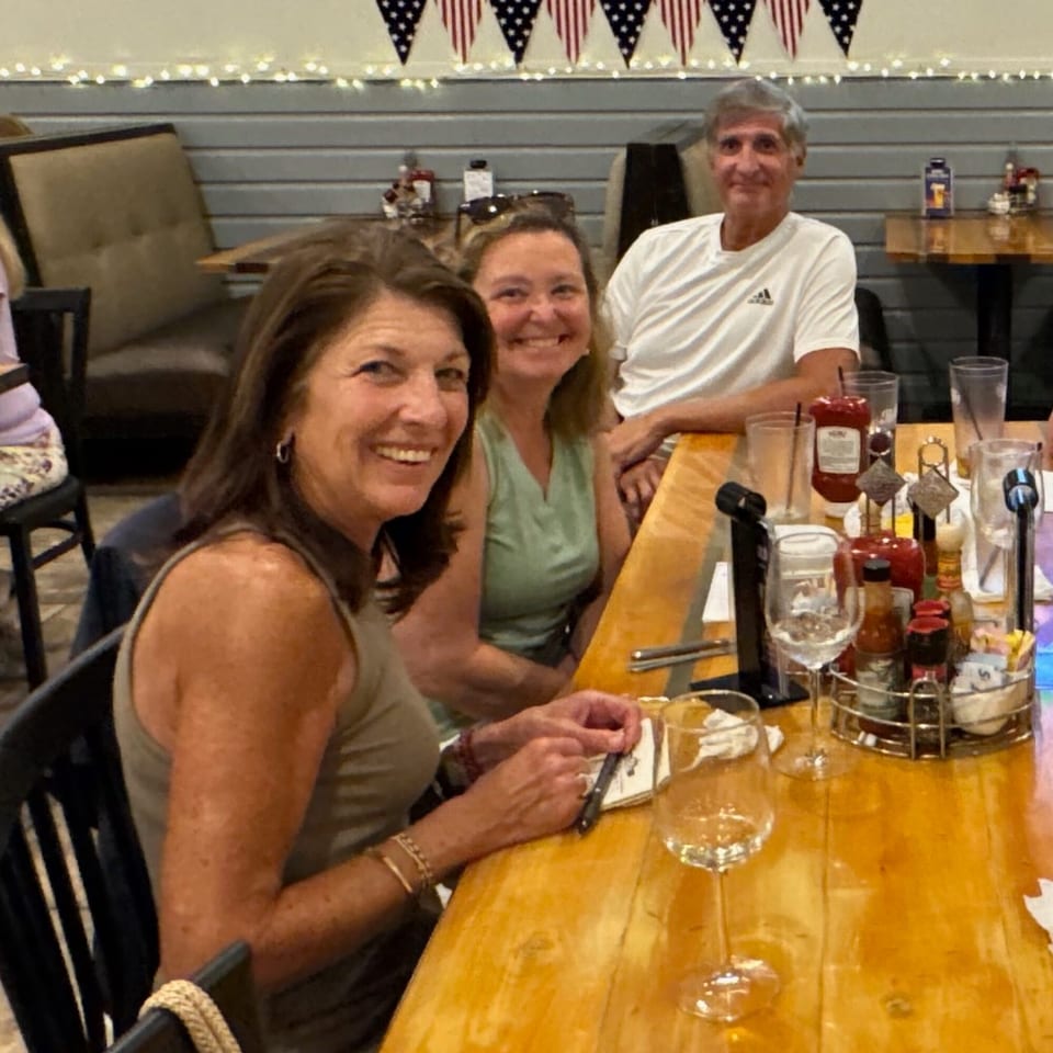 Three happy diners, two women and one man, seated at a wooden table in The Salted Rim.