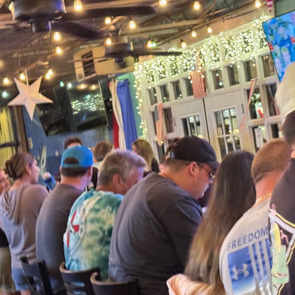 Patrons seated at a bar, with string lights and American flags decorating the background.
