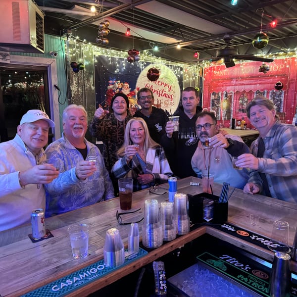 A group of people smiling and raising their drinks at a festive bar decorated for Christmas.