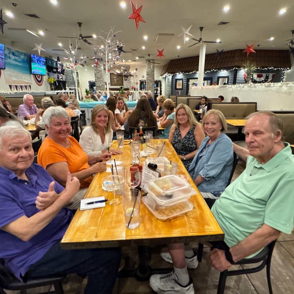 Group of six adults smiling at a long wooden table in a festive Mexican restaurant.