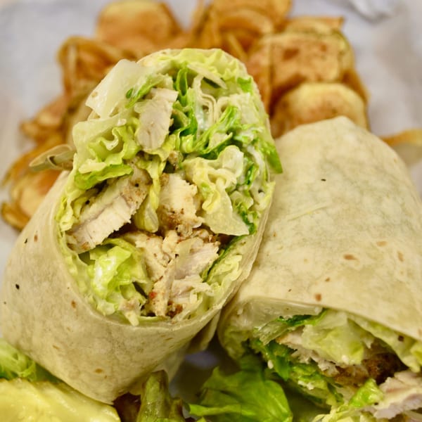 Two chicken Caesar wraps, cut in half, with a side of golden brown potato chips.