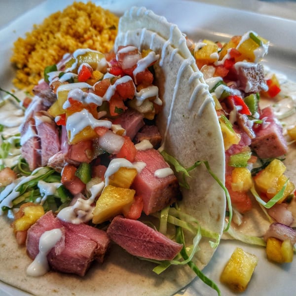 Two Salted Rim tacos filled with meat, pineapple salsa, and drizzled with white sauce, alongside yellow rice.