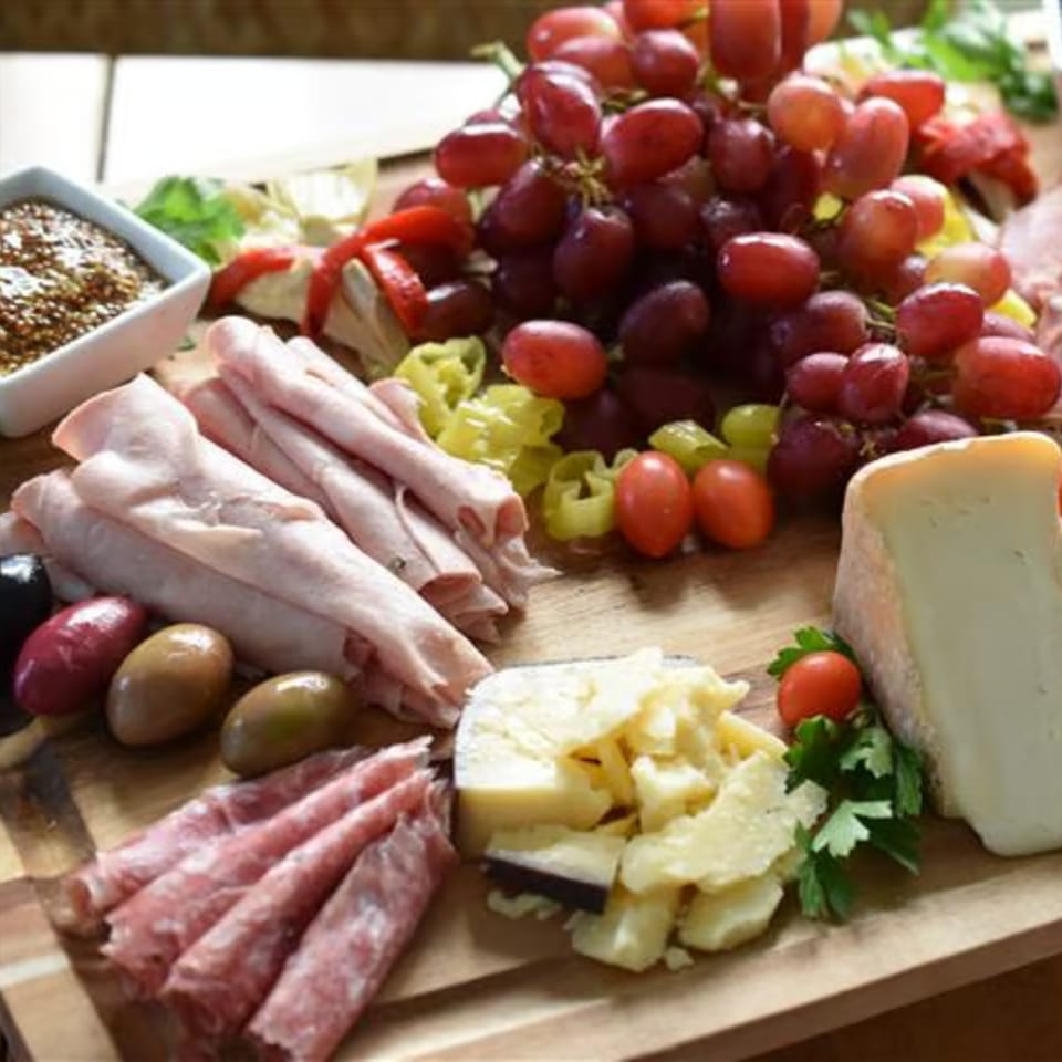 A charcuterie board with grapes, cheeses, sliced meats, olives, cherry tomatoes, and mustard.