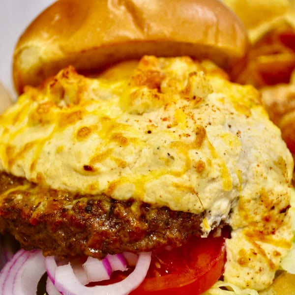 Close-up of a burger with a thick layer of melted cheese, tomato, and red onion.