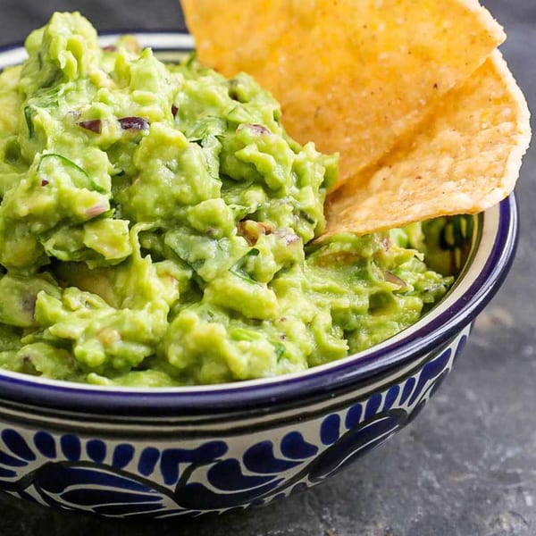 Fresh guacamole in a blue and white patterned bowl with a tortilla chip dipped in it.